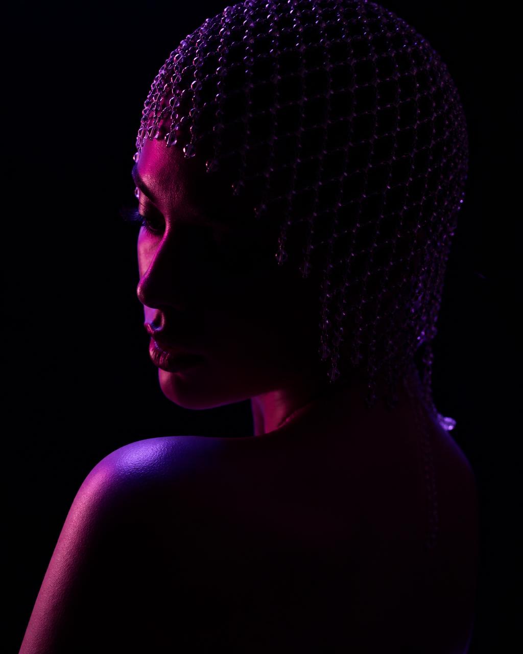 Profile portrait of a performer in crystal headpiece under violet light
